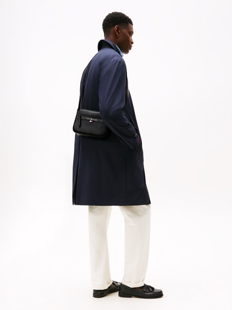 Navy coat, white pants, and black shoes. The coat features a high collar and a matte texture. A small black crossbody bag is worn.