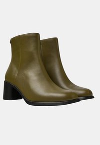 Botines de cuero verde oliva con una textura suave, punta redondeada y un tacón negro apilado. Diseño sencillo sin decoraciones visibles.