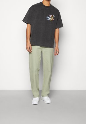 Szary, oversize'owy t-shirt z wielokolorowym logo "Worst Behavior", w połączeniu z jasnooliwkowymi, luźnymi spodniami i białymi trampkami.