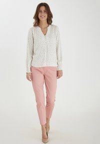 Vit blus med små färgglada blommönster, V-ringning och elastiska ärmar; tillsammans med ljusrosa figurnära byxor och beige klackar.