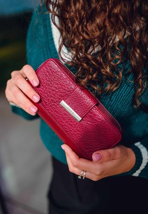 Red leather wallet featuring a textured surface, silver hardware with the brand name "VUCH," and a zip closure, held in a hand.