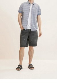 Camisa de manga corta de cuadros azules sobre una camiseta blanca, combinada con pantalones cortos de mezclilla oscuros hasta la rodilla y sandalias negras. Estilo sencillo y casual.