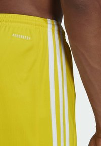 Geel sportshorts van lichtgewicht materiaal met witte verticale strepen en de tekst "AEROREADY" nabij de tailleband.