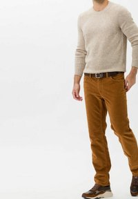 Bruna kordbyxor, beige texturerad tröja, brun bälte och flerfärgade sneakers. Outfiten har en avslappnad passform och ribbade detaljer.