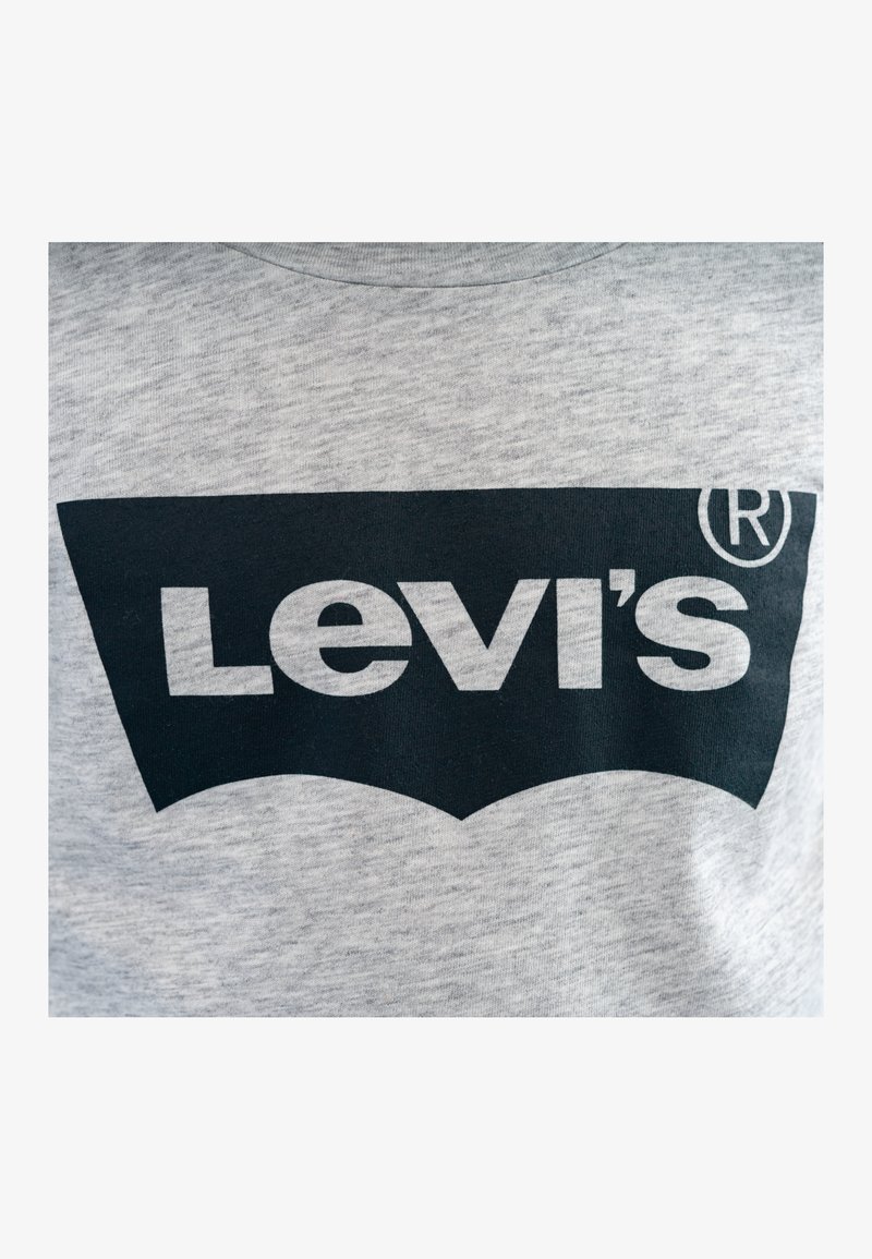 Camiseta gris con un gran logo negro de Levi's en el centro, con el símbolo de marca registrada en la esquina superior derecha. Textura suave de algodón.