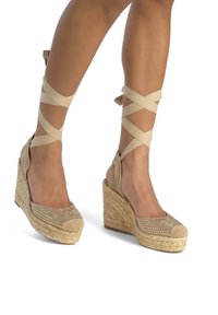Espadrillas beige con zeppa, suola in juta intrecciata, decorate con strass sulla punta. Cinghie di tessuto incrociate avvolgono la caviglia.