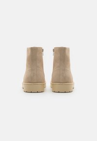 Botines de ante beige con una textura suave, detalle de cremallera lateral y una suela de goma gruesa y con patrón. Diseño minimalista sin adornos.