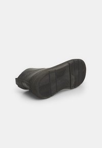 Must musta kummi tallaga, tekstureeritud soontega, kergelt tõstetud kontsaga ja siledapoolse servaga. Omab kumerat kujundust ja minimalistlikku disaini.