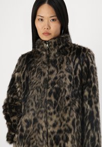 Veste en fausse fourrure avec un col montant au motif léopard. Présente une fermeture éclair et une surface douce et texturée dans des tons de marron et noir atténués.