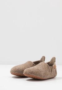 Chaussons en feutre marron avec une coupe basse, des panneaux latéraux élastiques et des semelles en caoutchouc. Texture douce, forme arrondie et design minimaliste.