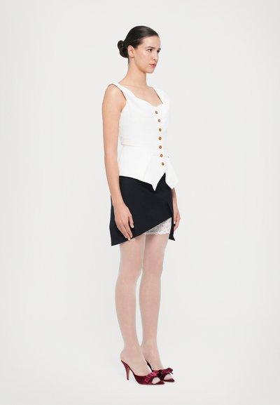 Hvid ærmeløs peplum top med orange knapper, parret med en sort mini-nederdel med asymmetrisk kant. Røde hæle med sløjfer.