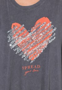 T-shirt grigia con un grande cuore corallo realizzato in paillettes, con la scritta "DIFFONDI il tuo amore" sotto in un font a contrasto.