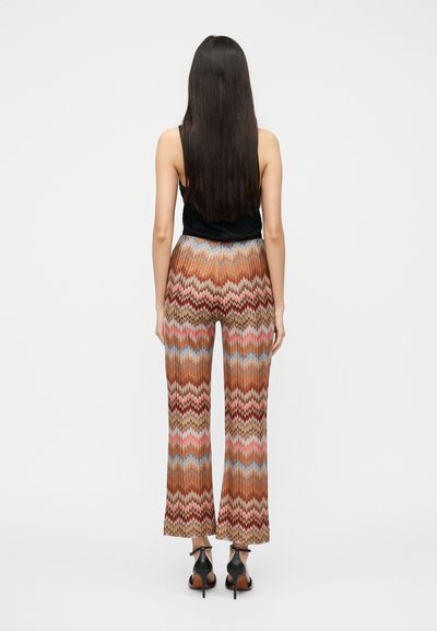 Pantalon large multicolore avec un motif en zigzag dans des tons de marron, rose et bleu ; associé à un haut sans manches noir et des talons noirs.