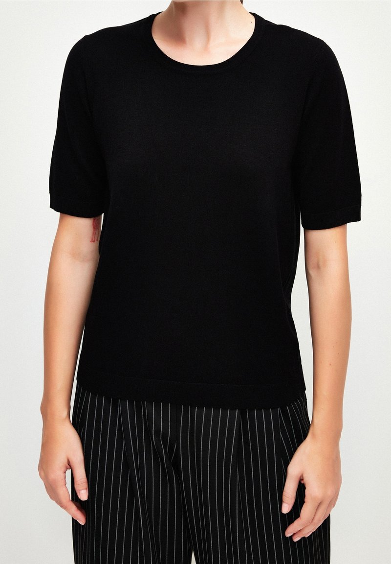 Černý krátký pletený top s kulatým výstřihem a hladkou texturou. Volný střih, v kombinaci s pruhovanými kalhotami s vysokým pasem.
