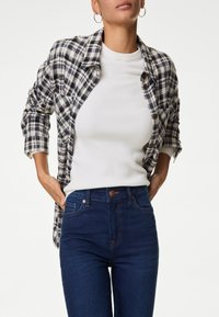 Rutig flanellskjorta i marinblå och vit, bärs över en ribbad vit topp. Högmidjade blå jeans med en bronsknapp, åtsittande silhuett.