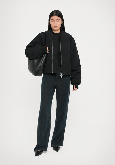 Chaqueta bomber negra recortada con cremallera, puños acanalados y una tela texturizada. Combinada con jeans oscuros de pierna ancha y una bolsa de mano negra.