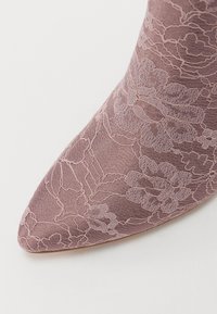 Pantof cu vârful ascuțit dintr-un material mauve, cu un overlay din dantelă florală. Prezintă o suprafață texturată și o strălucire subtilă, creând o apariție elegantă.