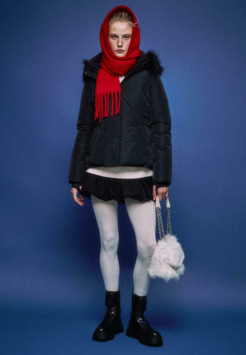 Črno obložena jakna z rjavo-puhasto kapuco, rdeča ruta, bel pulover, črna krilo, bele gamaše in črni bojevski škornji. Drži puhasto belo torbico.