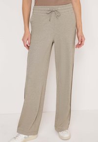 Pantalon de survêtement gris clair avec une taille à cordon, fentes latérales et coupe décontractée, présentant une texture lisse et un éclat subtil.