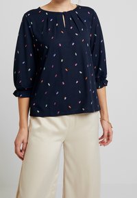 Námořnická blůza s kulatým výstřihem a detailem v podobě klíčové dírky. Obsahuje barevné vzory listů, tříčtvrteční rukávy a volný střih.