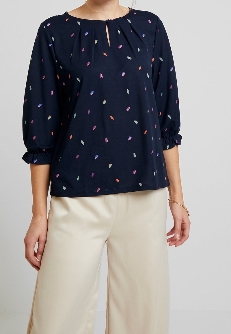 Námořnická blůza s kulatým výstřihem a detailem v podobě klíčové dírky. Obsahuje barevné vzory listů, tříčtvrteční rukávy a volný střih.