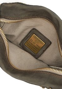 Interno di una borsa in pelle marrone con cerniera dorata, rivestimento beige e un'etichetta del produttore con dettagli in rilievo. Texture liscia, design pratico.
