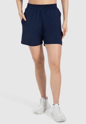 Shorts sportivi blu navy realizzati in un tessuto liscio, con una cintura flessibile e tasche laterali, indossati con sneakers bianche.