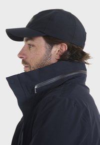 Marinejacke mit hohem Kragen, Reißverschlusstasche und Mütze. Der Stoff wirkt glatt mit dezentem Glanz und ist für den Außeneinsatz konzipiert.