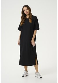 Black, short-sleeved maxi dress made of lightweight fabric, featuring side slits for ease of movement. Paired with white sneakers.