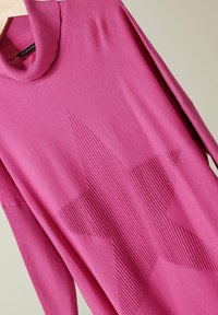 Maglione rosa a maglia con un design a stella a costine, colletto alto e maniche lunghe. La texture è liscia con una leggera lucentezza.
