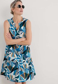 En ärmlös klänning med ett flerdelat kjol, prydd med ett djärvt geometriskt mönster i teal, blått, vitt och brunt, tillverkad av lättviktig tyg.