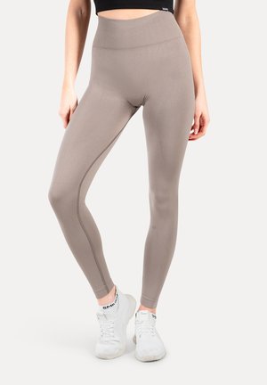 Leggings beiges taille haute avec une texture lisse, présentant un détail de couture sur le côté et un tissu doux et extensible, associés à des baskets blanches.