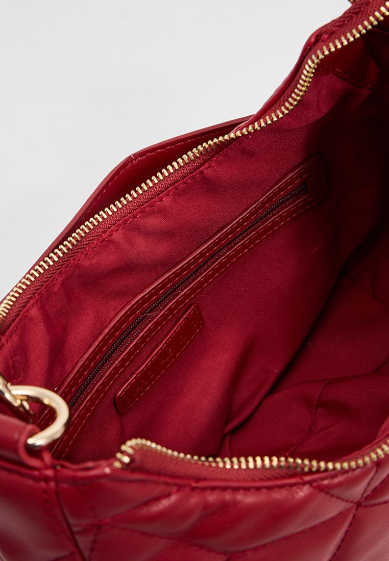 Roter gesteppter Handtaschen-Innenraum mit glattem Satin-Futter, einer Reißverschlusstasche und einem goldenen Reißverschlussakzent für einen einfachen Zugriff.