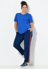 Blauw T-shirt met korte mouwen en V-hals, gecombineerd met marineblauwe broek met een oranje zijstreep. Gestyled met donkere sportieve schoenen.