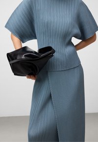 Plisserad ljusblå topp och matchande kjol, med breda ärmar och en sidofloss, tillsammans med en skrynklig svart läderväska.