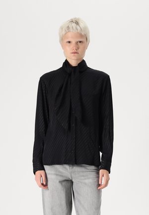 Svart knapp-up skjorta i texturerad tyg med knuten hals, försedd med vertikala ränder och långa ärmar, kombinerad med ljusgrå denim.