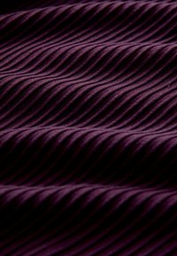 Fialová látka s textúrovaným vlnitým vzorom, jemná na dotyk, s alternujúcimi hrebeňmi, ktoré vytvárajú hĺbku a vizuálny záujem.