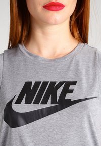 Grå bomullströja med en stor svart "NIKE"-logotyp och swoosh-design över bröstet, rund halsringning och korta ärmar.