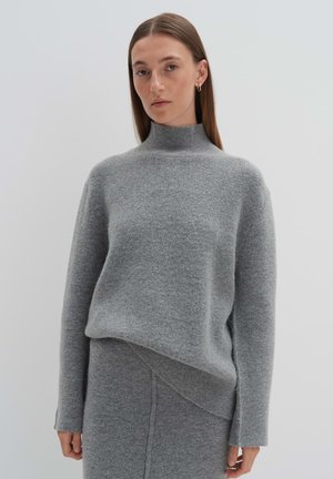 Pull à col roulé en laine grise, avec des manches longues et un ourlet légèrement asymétrique, présentant une texture douce et un design minimaliste.