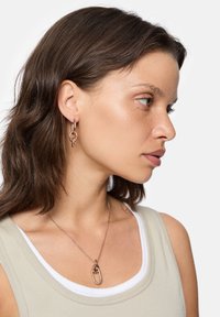 Øreringe i roseguld metal med sammenkoblede kædelinks, parret med en matchende pendantsmykke. Har en glat, reflekterende overflade.