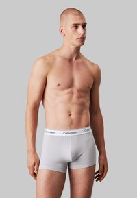 Grijze katoenen stretchboxershorts met een aansluitend design en een witte Calvin Klein-logo tailleband, getoond op een model tegen een neutrale achtergrond.