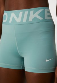 Aqua blå treningsshorts med en tykk, hvit logo-bånd i livet og en liten hvit Nike-svikt nederst til venstre. Glatt, elastisk materiale.