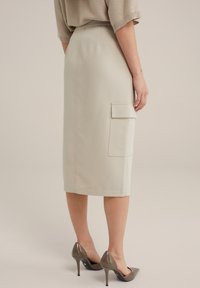 Beige skräddarsydd midi kjol med sidofickor, slät textur och kontrasterande sömmar, ihopsätt med glansiga högklackade skor.