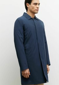 Granatowy płaszcz o średniej długości, prostym kroju, z zapięciem na guziki i kieszeniami bocznymi. Gładka faktura i klasyczny fason kołnierza.