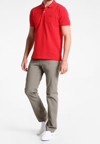 Rød polo-shirt med krave og korte ærmer, parret med lysegrå bukser og hvide slip-on sko.