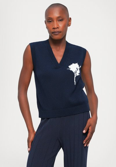 Marineblå ermeløs strikkegenser med V-hals og ribbestrikket kant, med et strukturert hvitt blomsterdesign på venstre side.