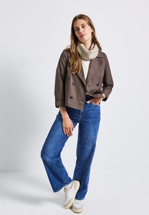 Brun cropped dobbeltbrystet jakke, beige cowl-neck sweater, blå vidde jeans og hvide sneakers med beige accenter.