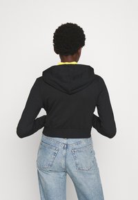 Sudadera negra recortada con capucha ajustable, confeccionada en tela suave, con cintura entallada y mangas largas, combinada con vaqueros azul claro.