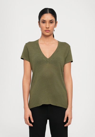 Oliwkowy T-shirt z dekoltem w kształcie litery V i krótkimi rękawami, wykonany z teksturowanej tkaniny, z zaokrąglonym dołem i luźnym krojem. Na sobie ma czarne spodnie.