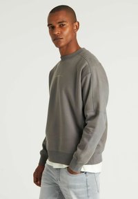 Grå sweatshirt med rund halsudskæring, afslappet pasform,ribbenede manchetter og et diskret logo på brystet. Bæres med lysegrå jeans.